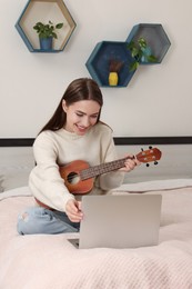 Happy young woman learning to play ukulele with online music course at home. Time for hobby