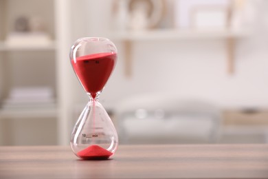 Photo of Hourglass with red flowing sand on table against blurred background. Space for text