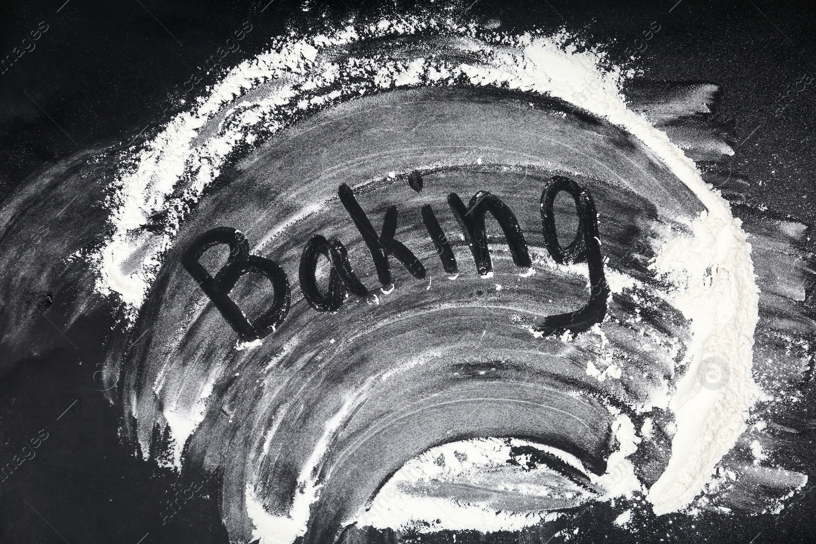 Photo of Word BAKING written on flour scattered over black table, top view