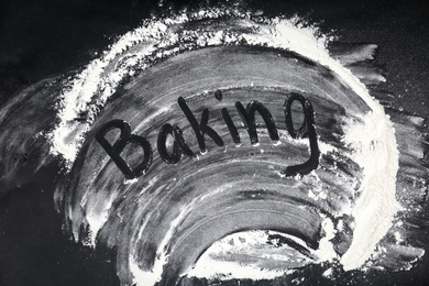 Word BAKING written on flour scattered over black table, top view