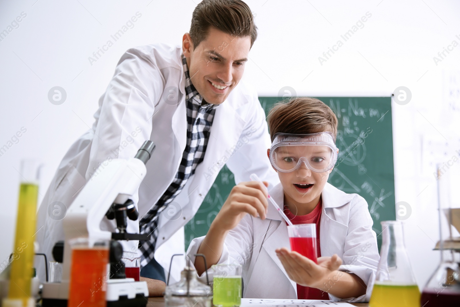 Photo of Teacher with pupil making experiment at table in chemistry class