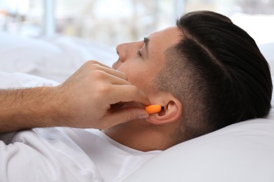 Photo of Man inserting foam ear plugs in bed, closeup