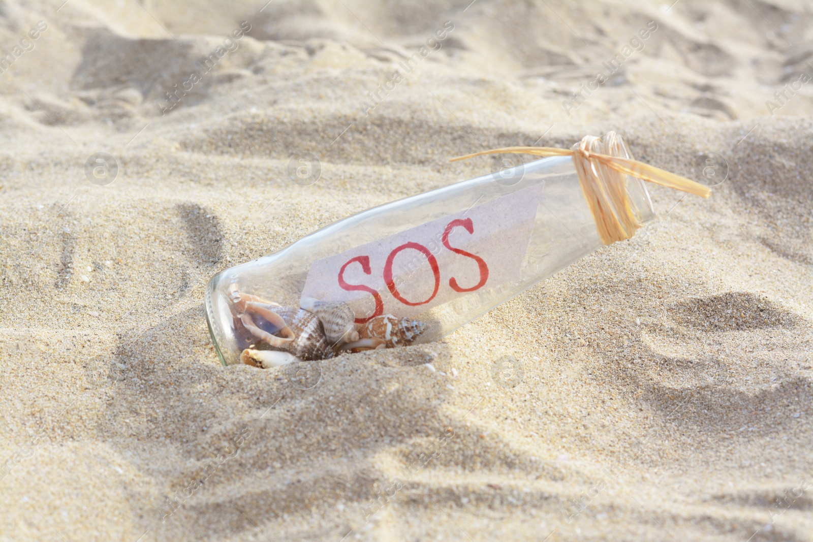 Photo of Glass bottle with seashells and message SOS on sand