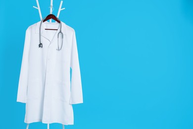 White medical uniform and stethoscope hanging on rack against light blue background. Space for text