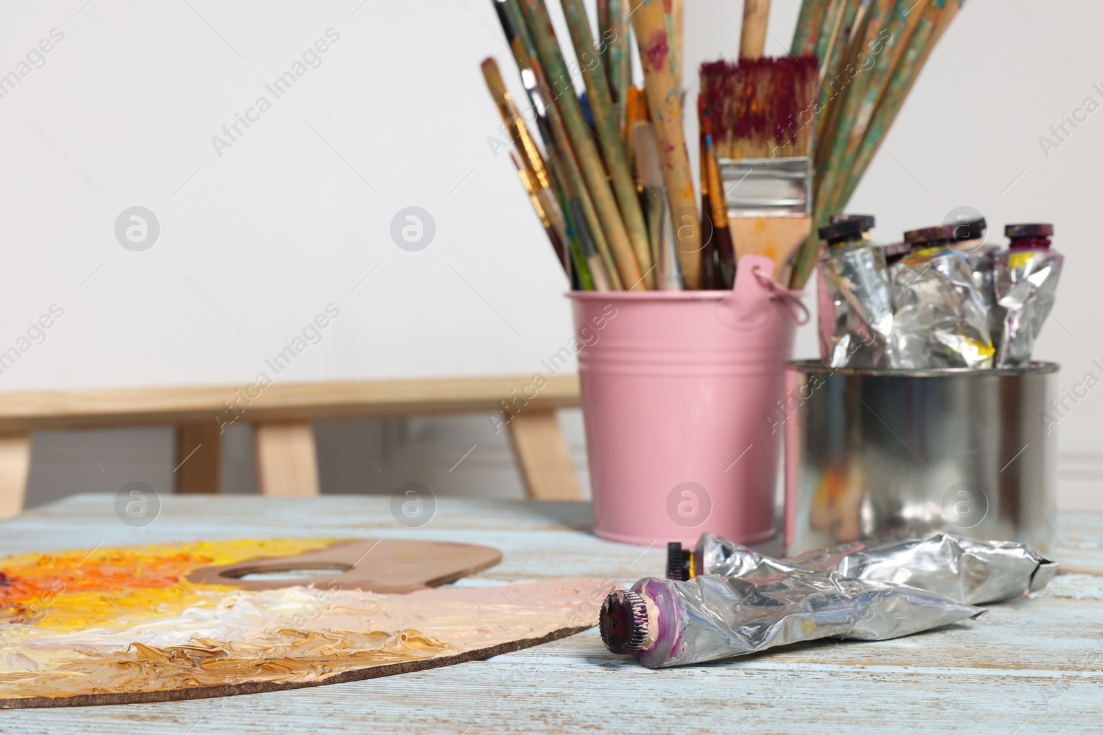 Photo of Easel with blank canvas and different art supplies on wooden table, closeup