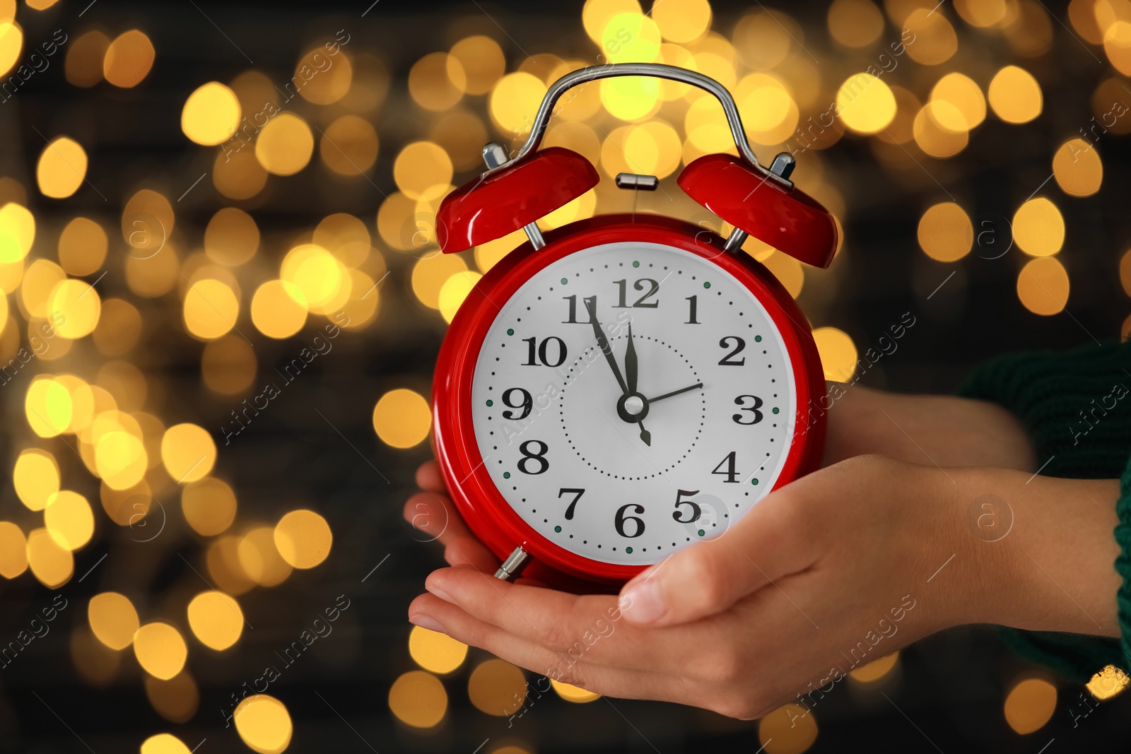 Photo of Woman holding alarm clock against blurred lights, closeup. New Year countdown