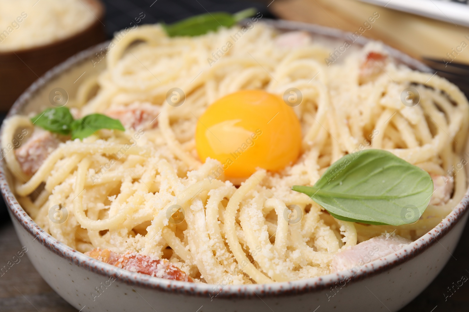 Photo of Tasty pasta Carbonara with basil leaves and egg yolk in bowl, closeup