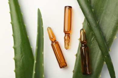 Photo of Skincare ampoules and aloe leaves on white background, flat lay