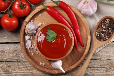 Photo of Delicious ketchup in bowl, products and spices on wooden table, flat lay. Tomato sauce