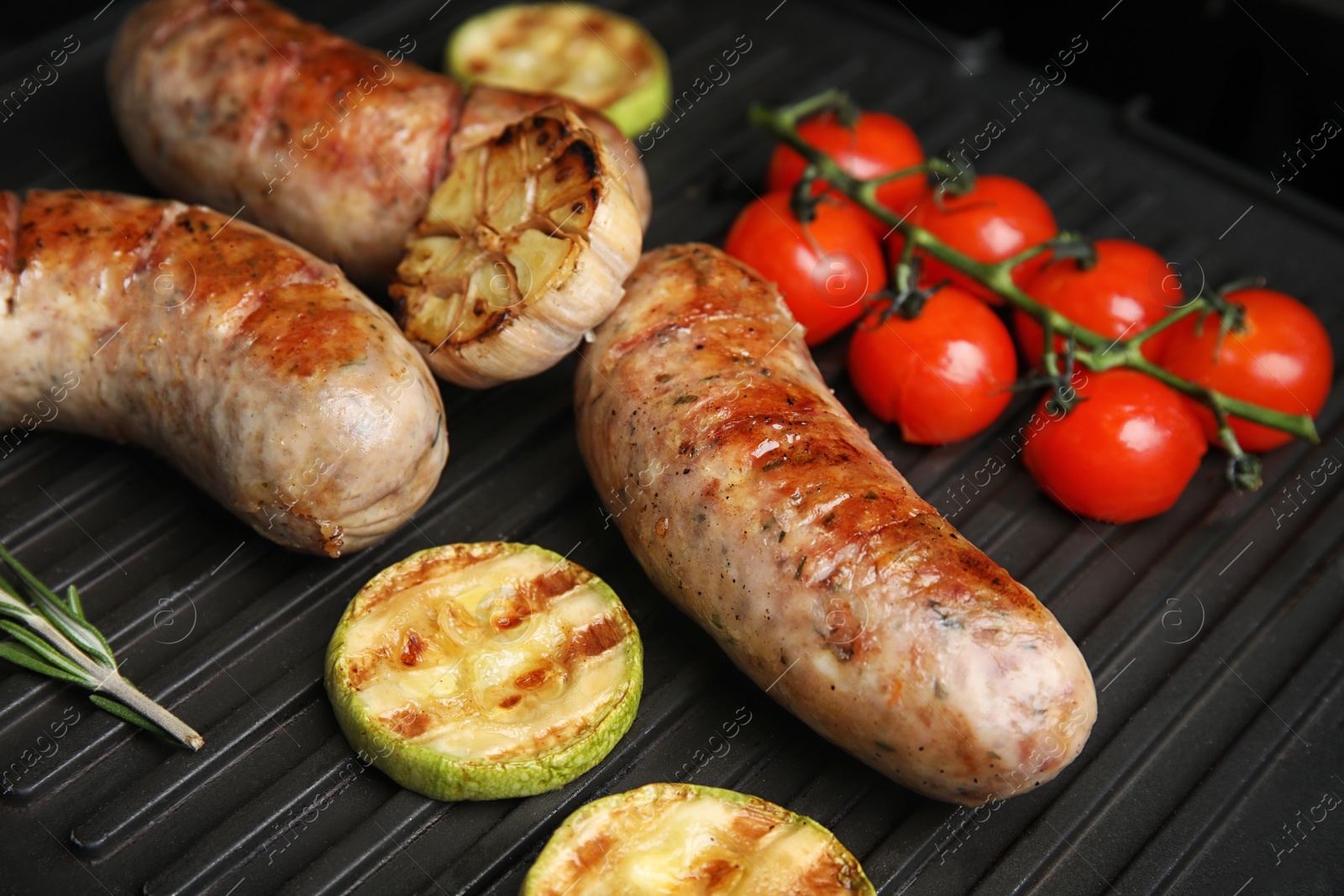 Photo of Cooking delicious fresh sausages with vegetables on modern grill