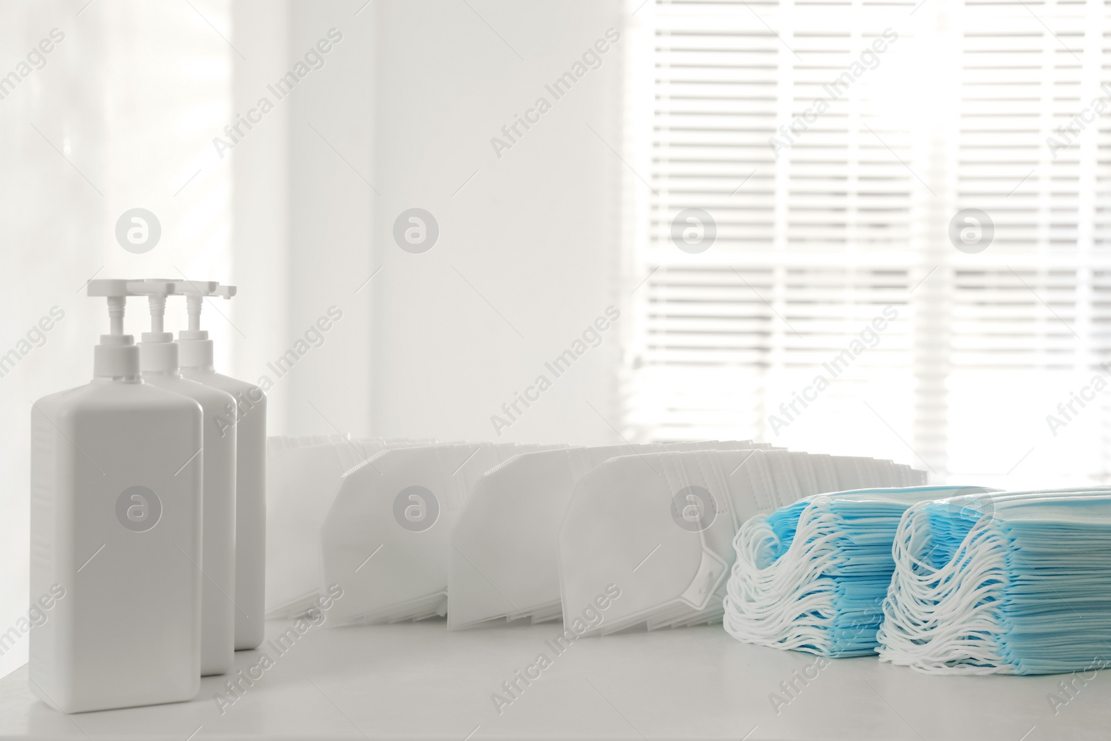 Photo of Hand sanitizers and respiratory masks on white table indoors. Protective essentials during COVID-19 pandemic