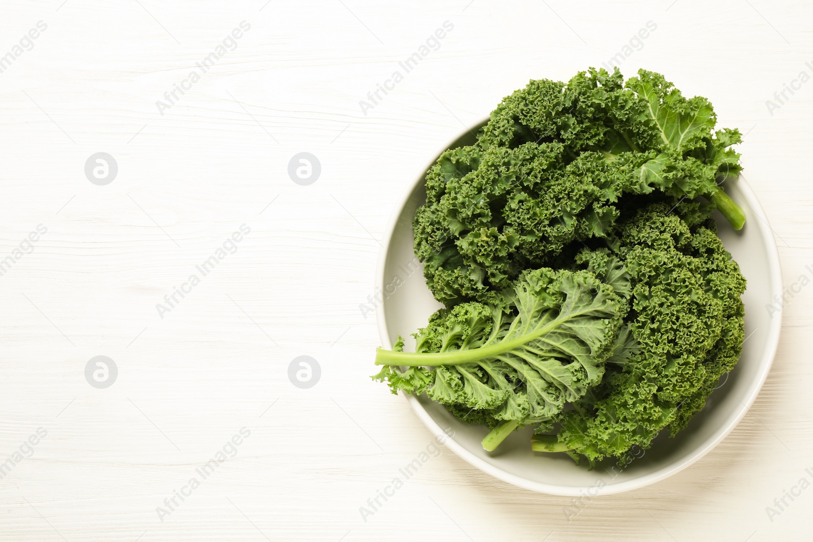 Photo of Fresh kale leaves on white wooden table, top view. Space for text