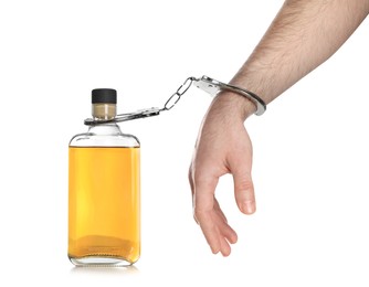 Photo of Addicted man in handcuffs with bottle of alcoholic drink on white background, closeup