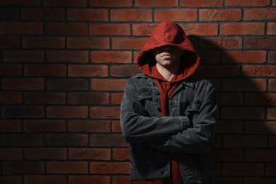 Photo of Thief in hoodie with crossed arms against red brick wall. Space for text