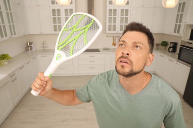 Photo of Man with electric fly swatter in kitchen. Insect killer