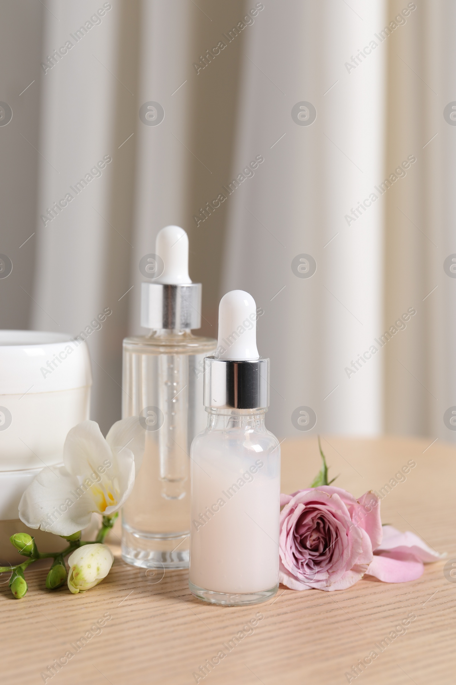 Photo of Bottles of cosmetic serum and beautiful flowers on wooden table