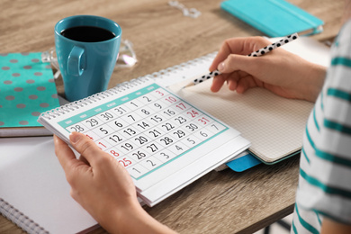 Photo of Woman making schedule using calendar at wooden table, closeup