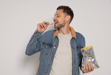 Handsome man eating potato chips on light grey background