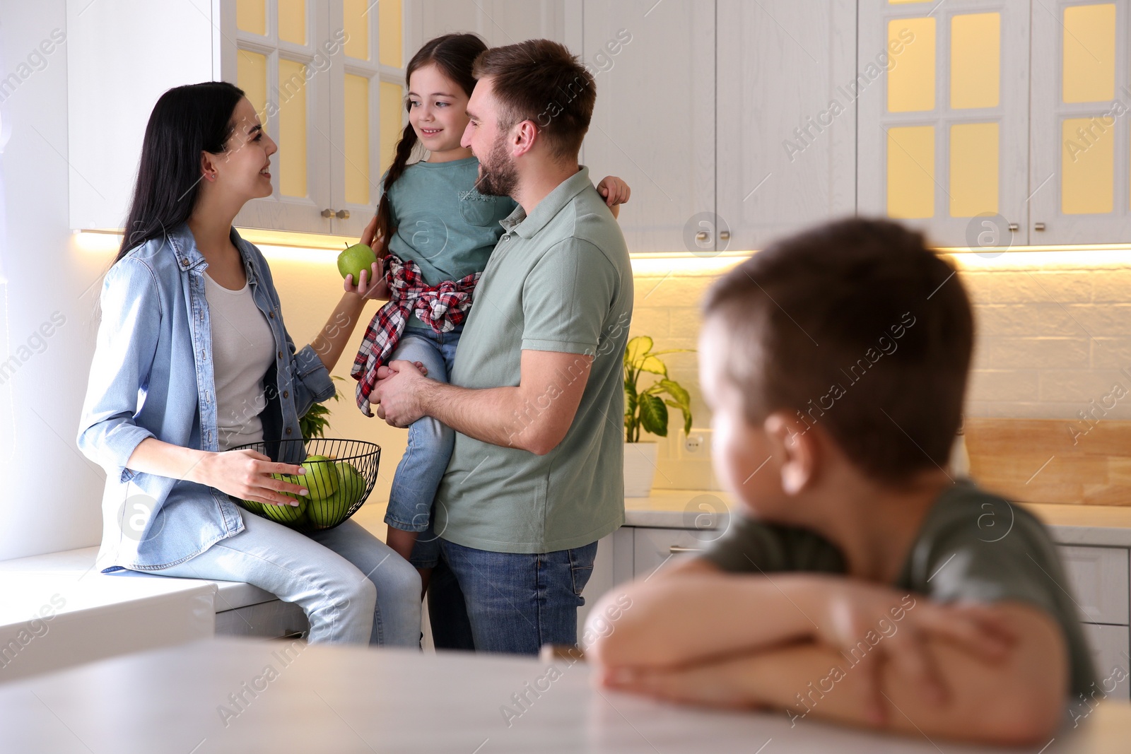 Photo of Unhappy little boy feeling jealous while parents spending time with his sister at home