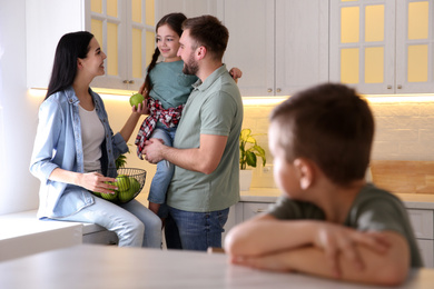 Unhappy little boy feeling jealous while parents spending time with his sister at home