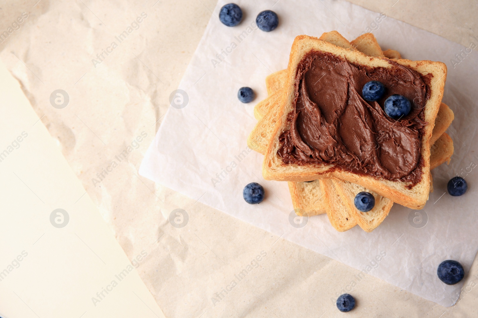 Photo of Tasty toast with chocolate paste and blueberries on parchment paper, flat lay. Space for text