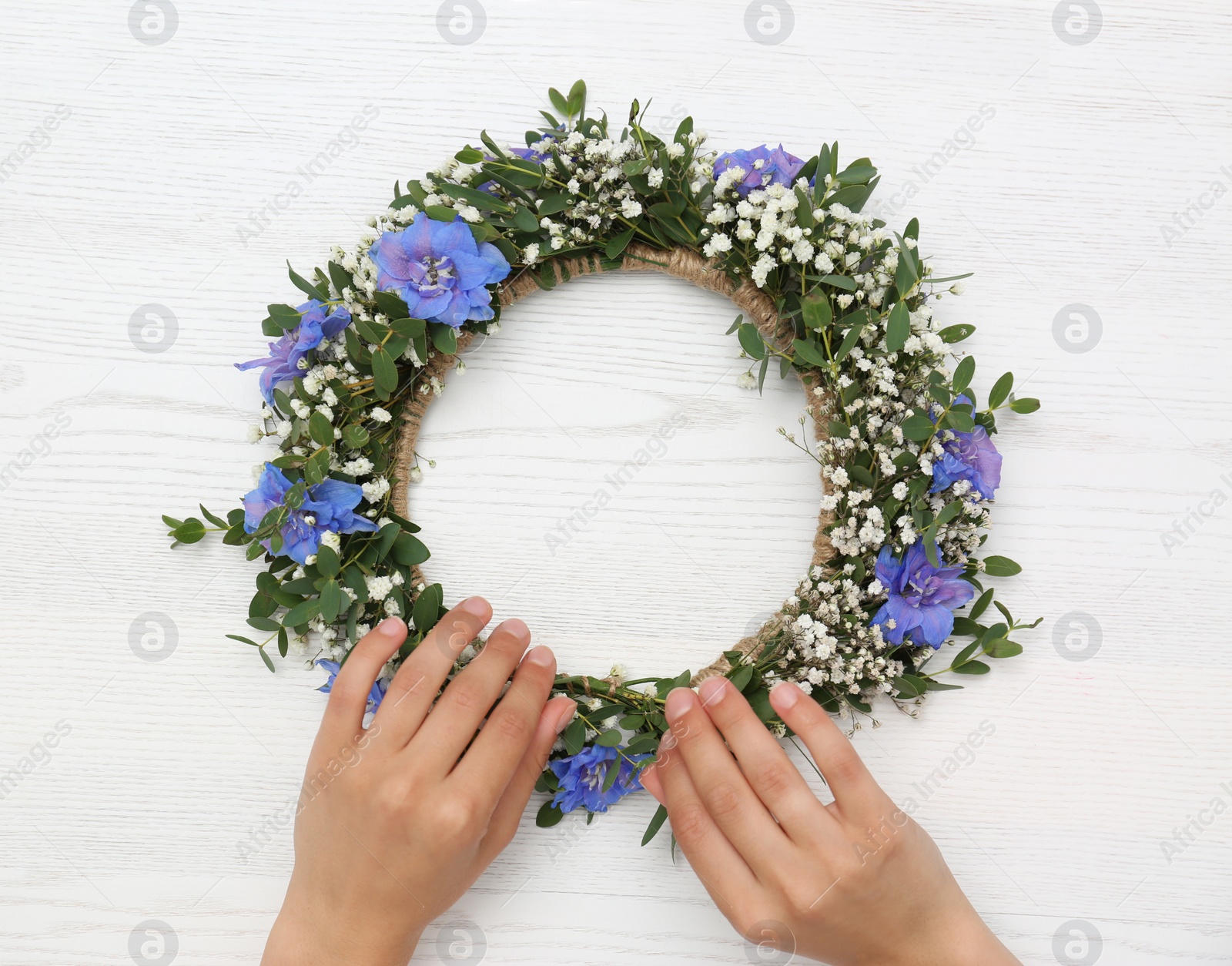 Photo of Woman making flower wreath at white wooden table, closeup