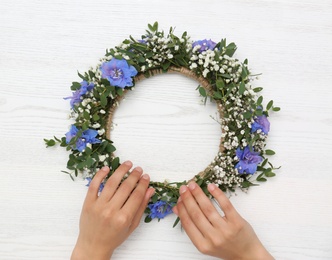 Woman making flower wreath at white wooden table, closeup