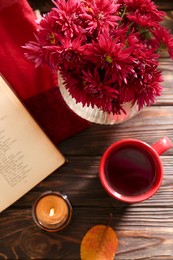Photo of Beautiful chrysanthemum flowers, cup of tea and book on wooden table indoors, flat lay
