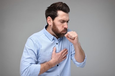 Photo of Sick man coughing on light grey background. Cold symptoms