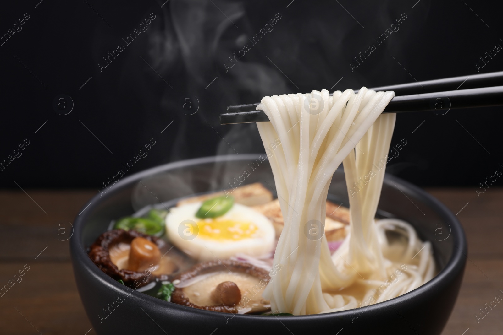 Image of Eating hot vegetarian ramen with chopsticks at table against black background, closeup