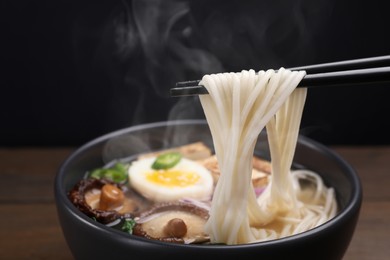 Image of Eating hot vegetarian ramen with chopsticks at table against black background, closeup