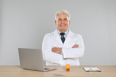 Photo of Professional pharmacist with laptop at table against light grey background