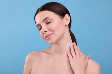 Photo of Beautiful woman with smear of body cream on her neck against light blue background