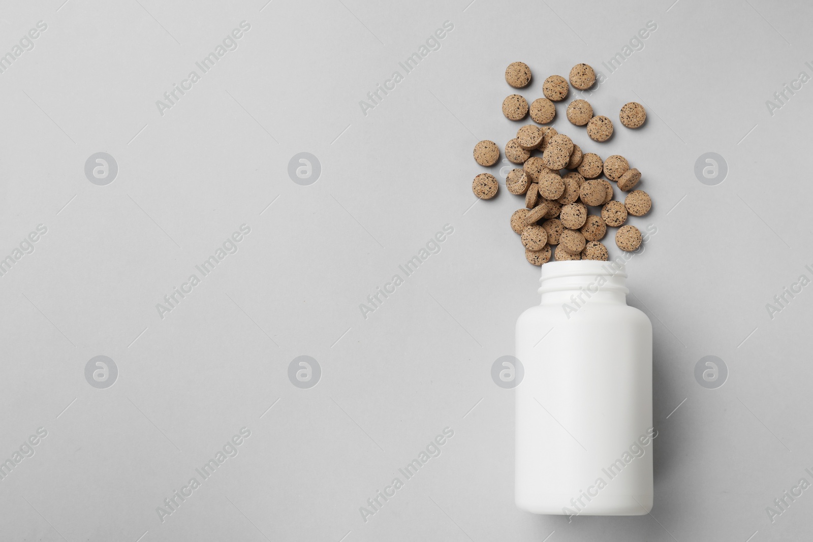 Photo of Vitamin pills and bottle on light grey background, top view. Space for text