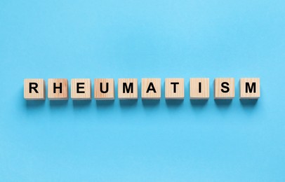 Photo of Word Rheumatism made of cubes on light blue background, top view