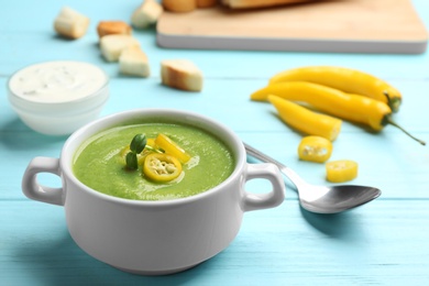 Photo of Bowl of broccoli cream soup with chili pepper served on blue wooden table. Space for text