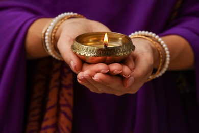 Photo of Woman holding lit diya lamp in hands, closeup. Diwali celebration