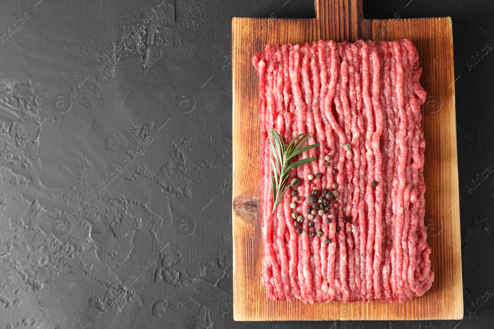 Photo of Raw ground meat, rosemary and peppercorns on black table, top view. Space for text