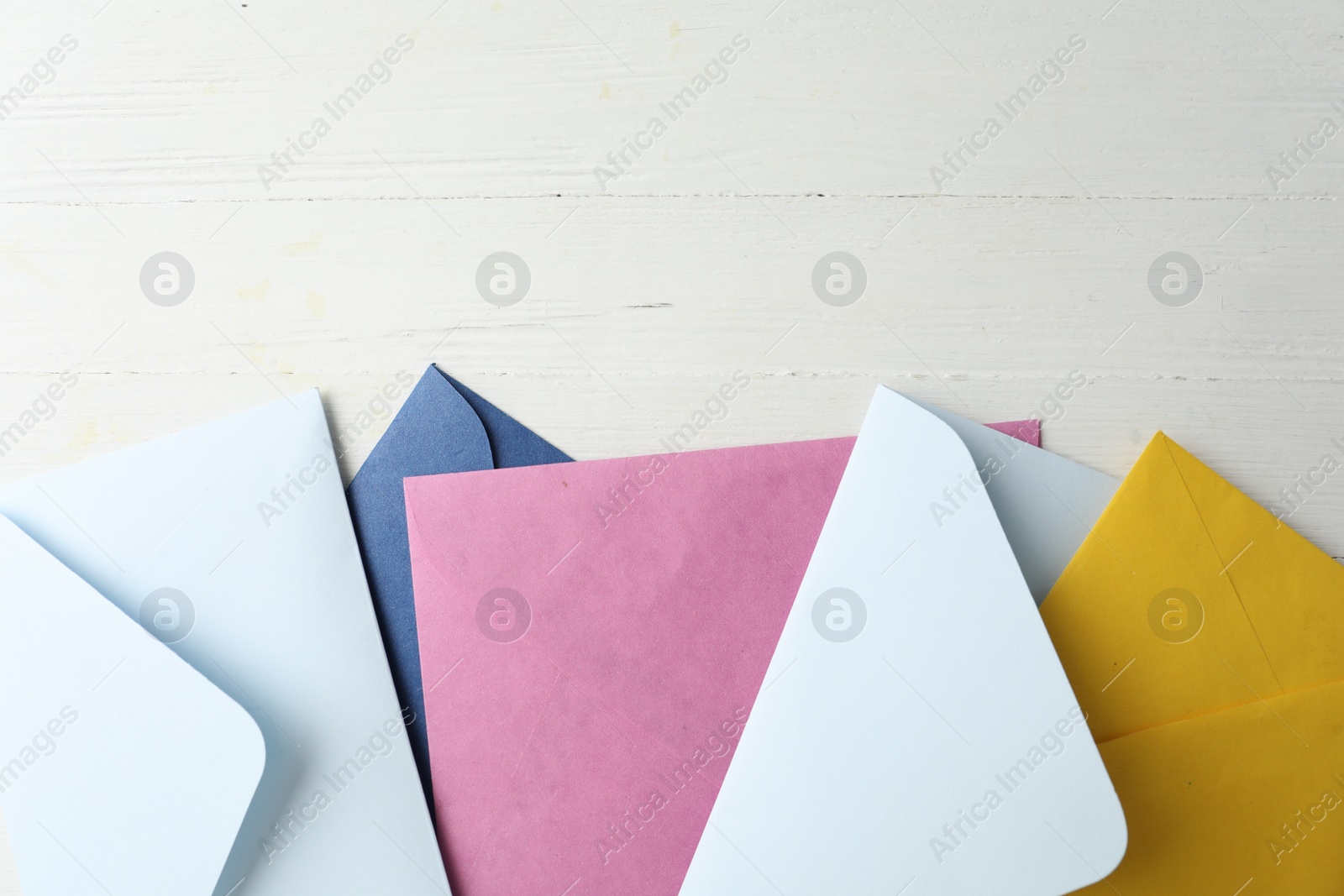 Photo of Colorful paper envelopes on white wooden table, flat lay. Space for text