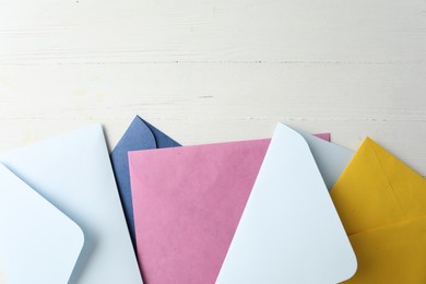 Colorful paper envelopes on white wooden table, flat lay. Space for text