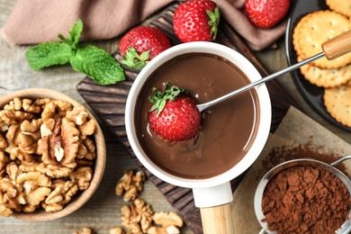 Photo of Dipping strawberry into fondue pot with milk chocolate on wooden table, top view