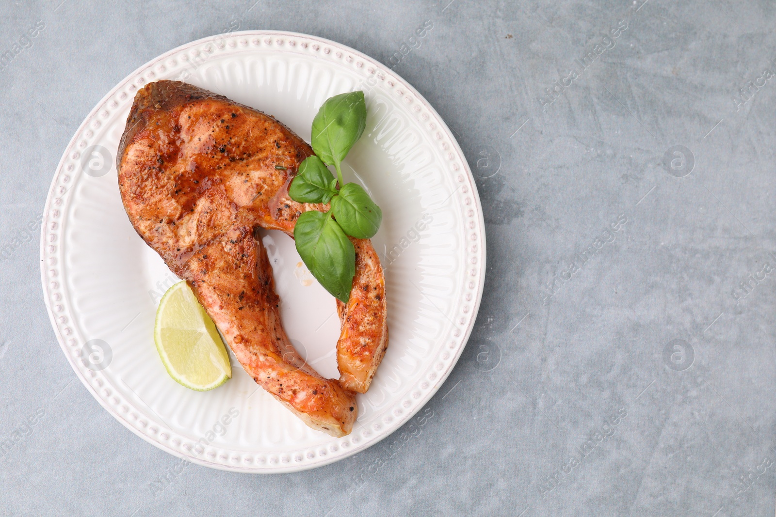 Photo of Freshly cooked fish, lime and basil on grey table, top view. Space for text