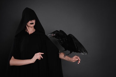 Photo of Mysterious witch with raven on black background