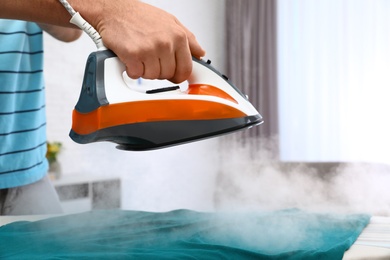 Photo of Man ironing clothes on board at home, closeup