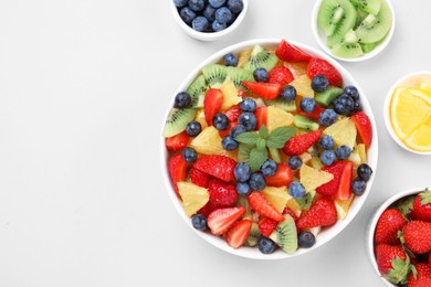 Photo of Yummy fruit salad in bowl and ingredients on light background, flat lay. Space for text