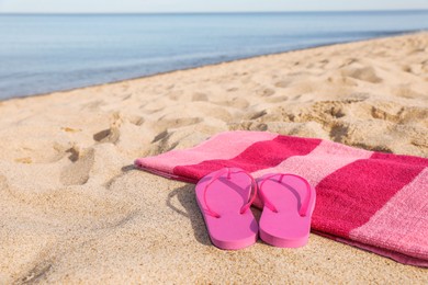 Photo of Beach towel and slippers on sand near sea, space for text
