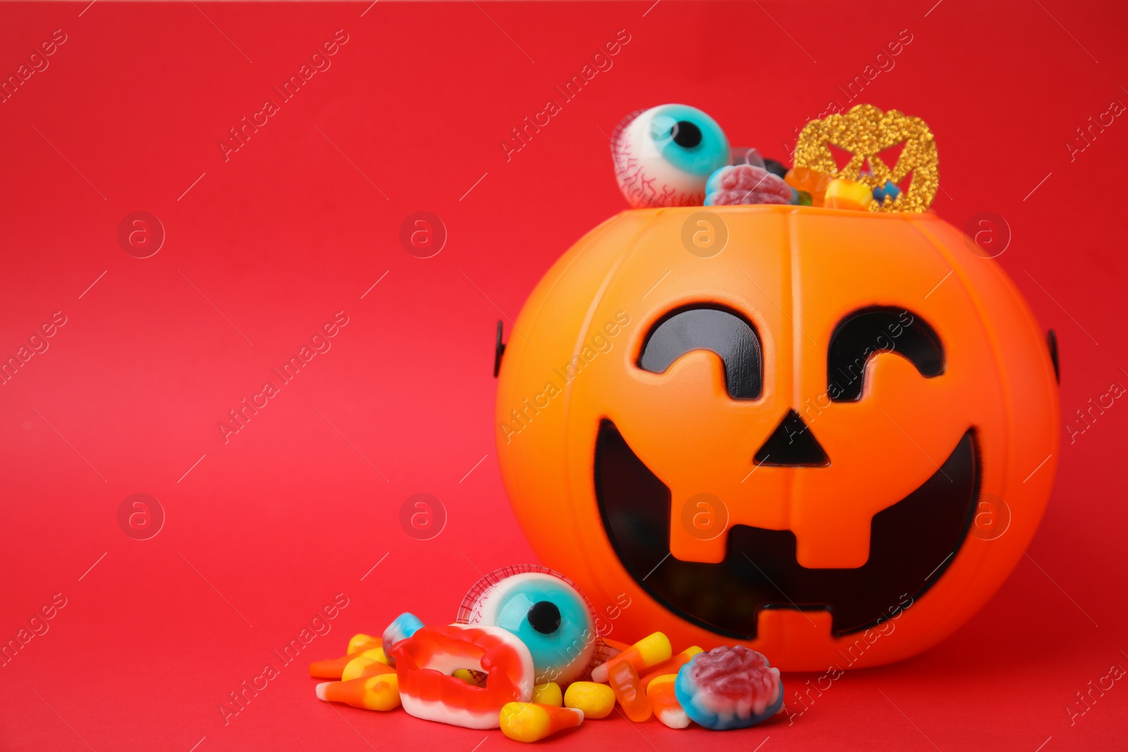 Photo of Halloween trick or treat bucket with different sweets on red background, space for text