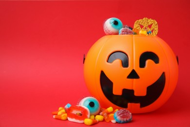 Halloween trick or treat bucket with different sweets on red background, space for text