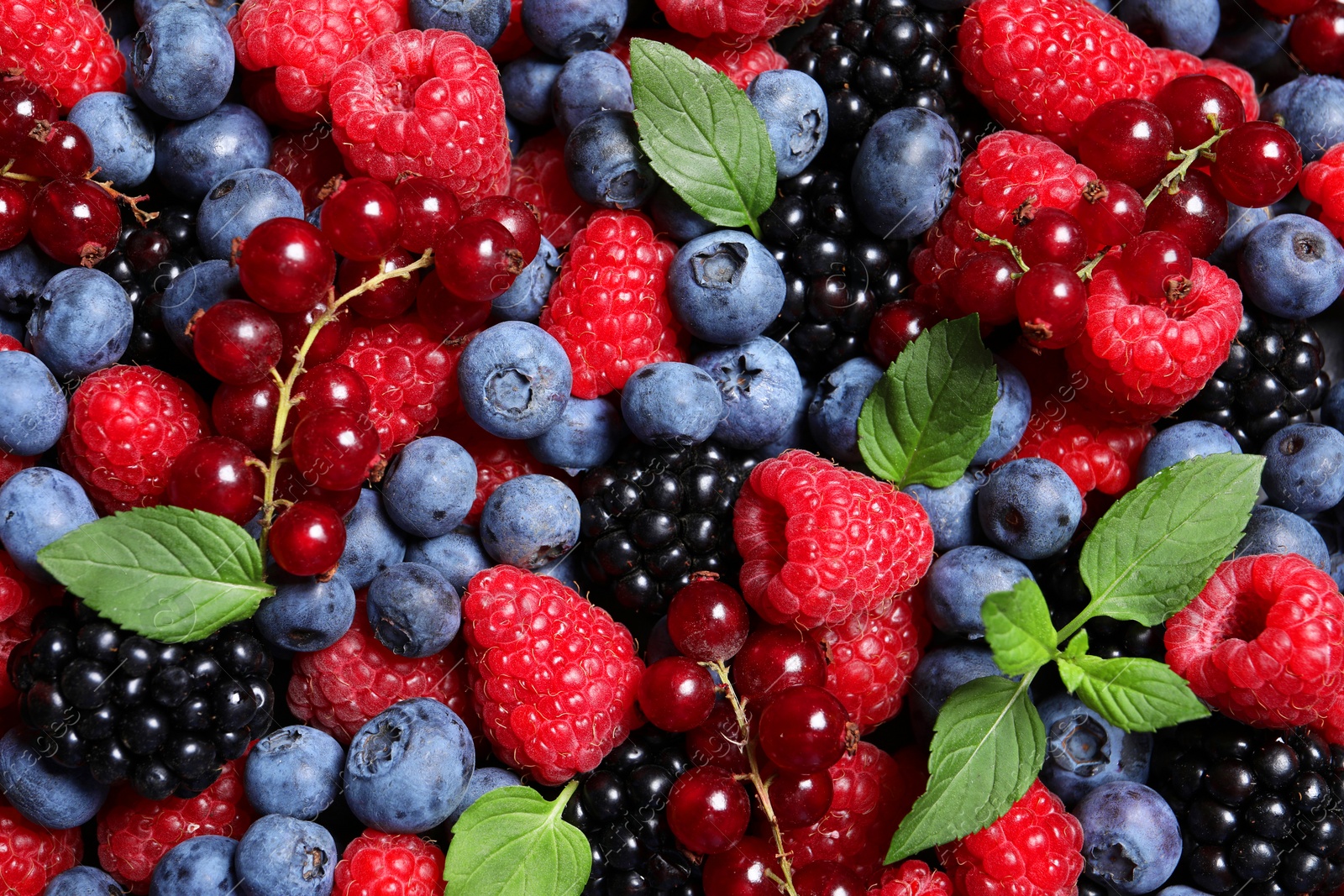 Photo of Assortment of fresh ripe berries with green leaves as background, top view
