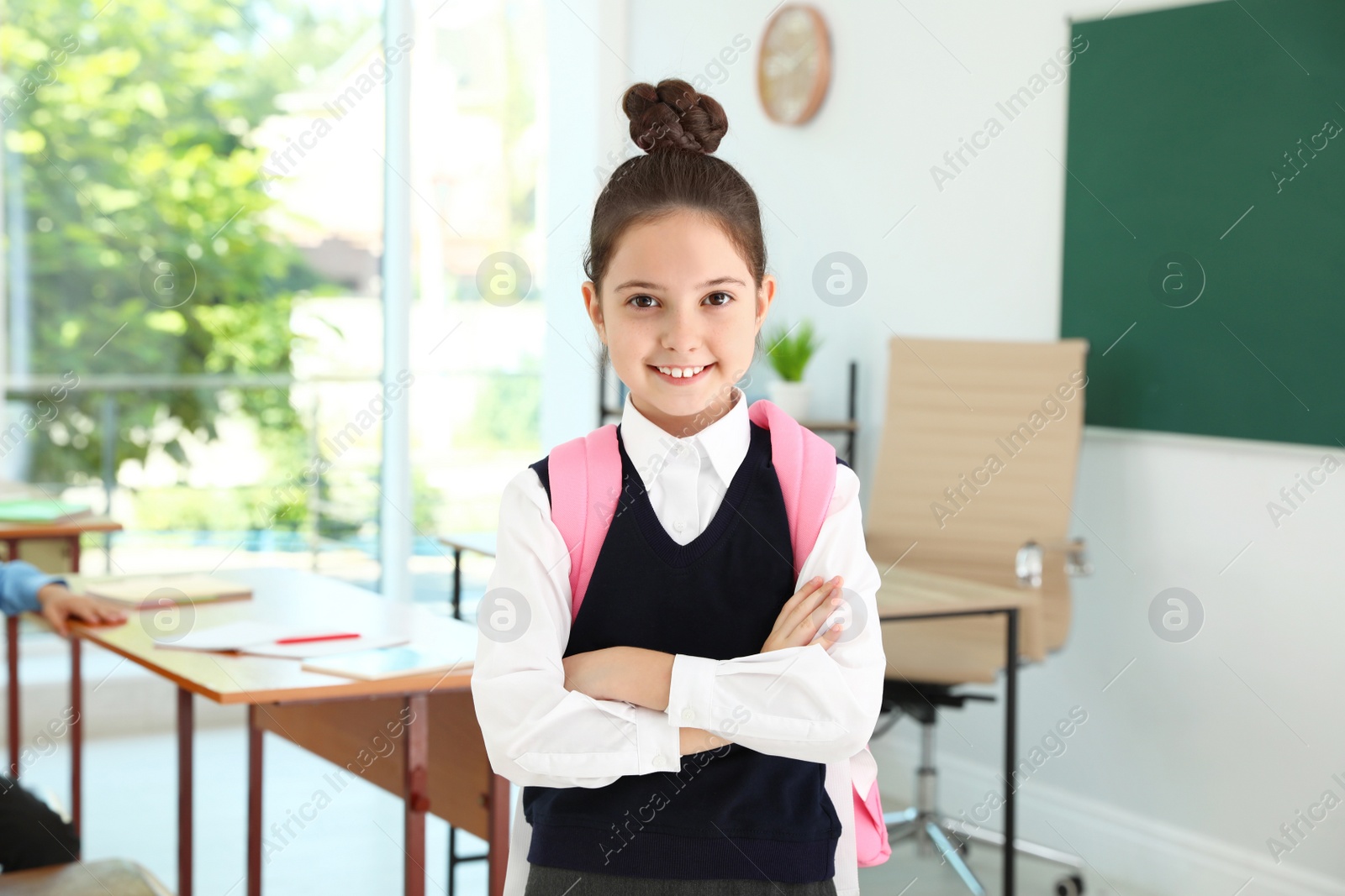 Photo of Girl wearing school uniform with backpack in classroom